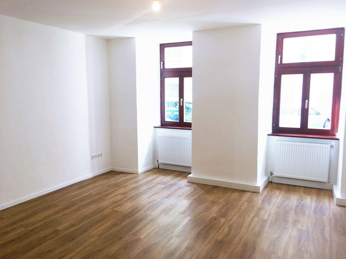 Heller Raum mit Laminatboden, weißen Wänden und zwei Fenstern, die eine angenehme Atmosphäre schaffen.