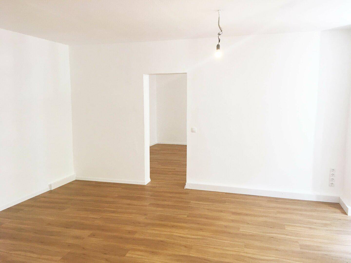 Geräumiger, heller Raum mit Laminatboden und weiß gestrichenen Wänden, bereit zur Einrichtung.