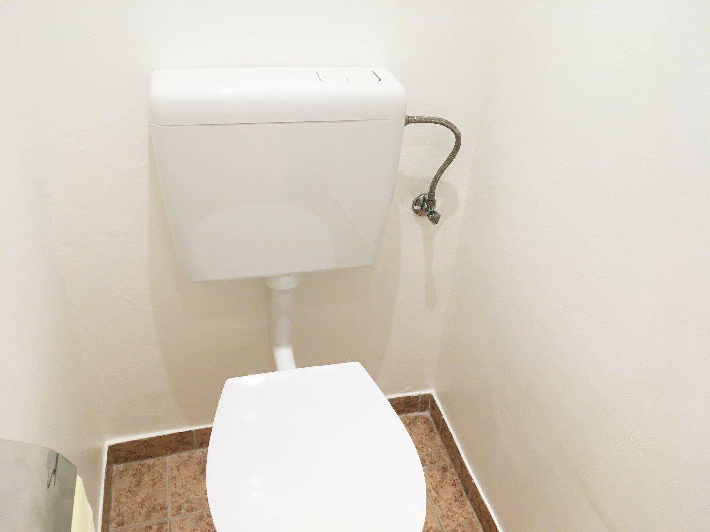Einfache Toilette mit weißer Keramik und gefliestem Boden, funktional und sauber.