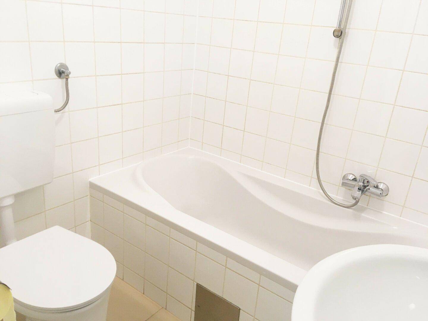 Badezimmer mit Badewanne, Toilette und weißen Wandfliesen, in einem gepflegten Zustand.