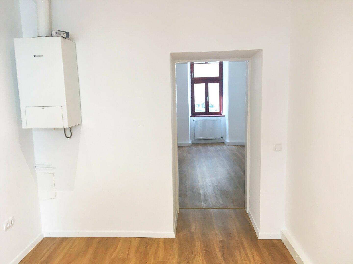 Heller Raum mit Laminatboden, weißen Wänden und einer Gastherme an der Wand, die für Wärme sorgt.