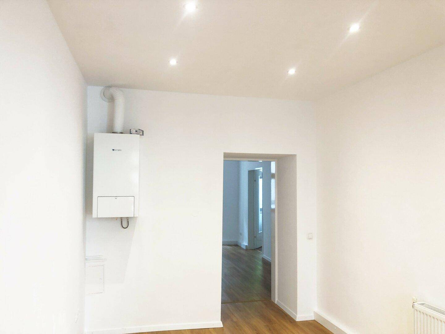 Heller Raum mit Laminatboden, weißen Wänden und einer sichtbaren Gastherme an der Wand.