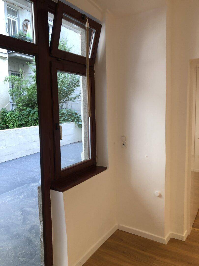 Heller Raum mit Laminatboden und einem Fenster, das einen Blick auf die grüne Umgebung bietet.