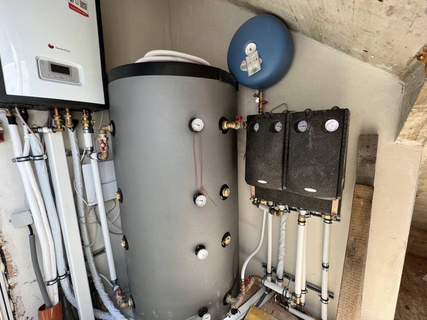 Heizungsanlage mit Warmwasserspeicher und komplexer Rohrinstallation in einem Technikraum.