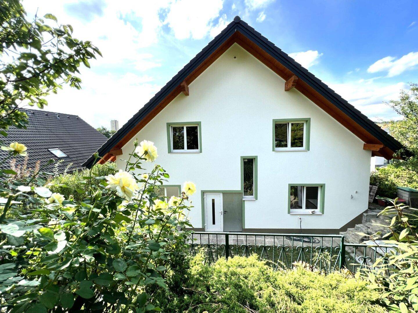 Vorderansicht des Hauses mit weißer Fassade, grünen Fensterrahmen und blühenden Rosen im Vorgarten.