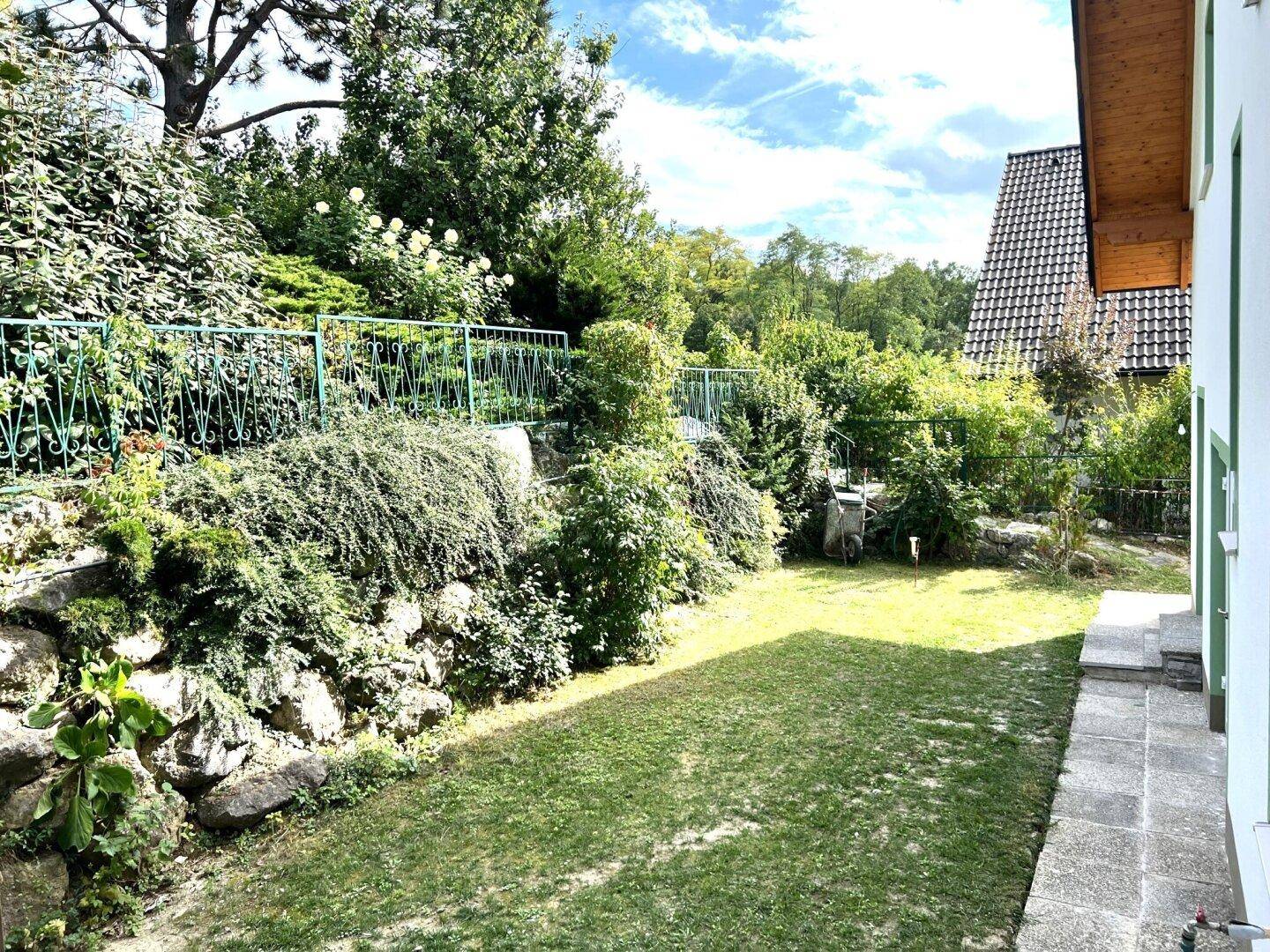 Gepflegter Garten mit Rasenfläche, einer Natursteinmauer und üppiger Bepflanzung.
