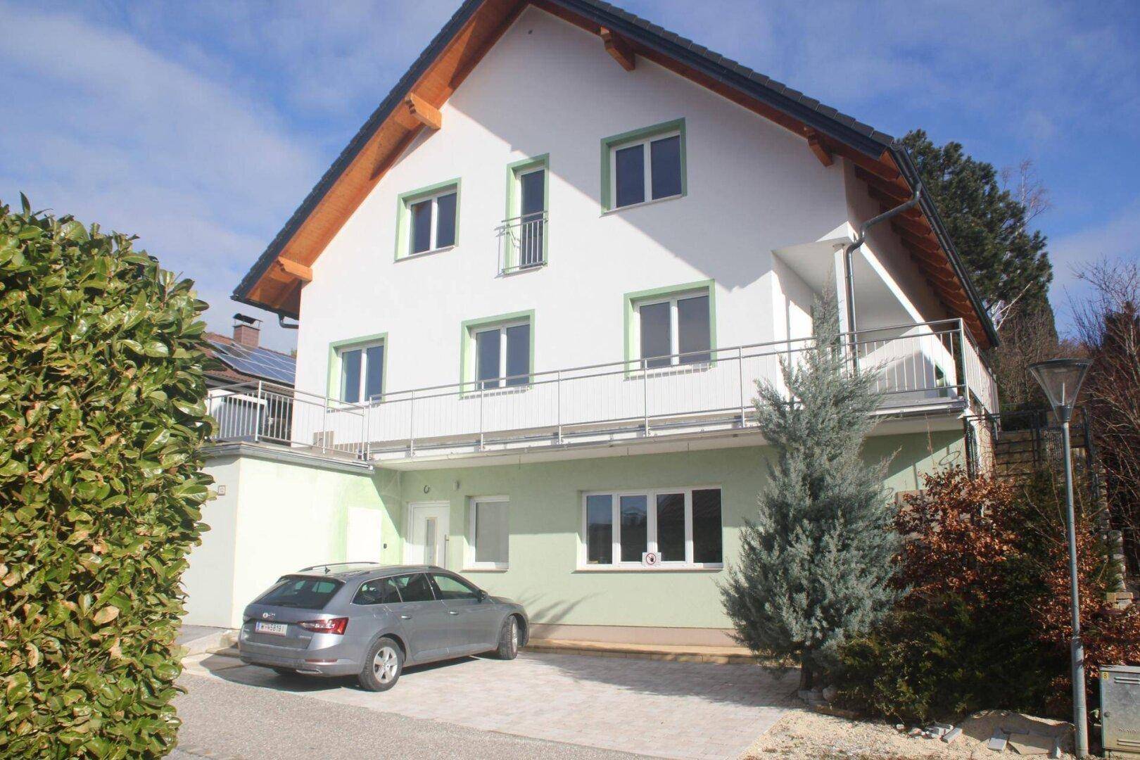 Seitenansicht des Hauses mit langem Balkon, gepflasterter Auffahrt und einem geparkten Auto.