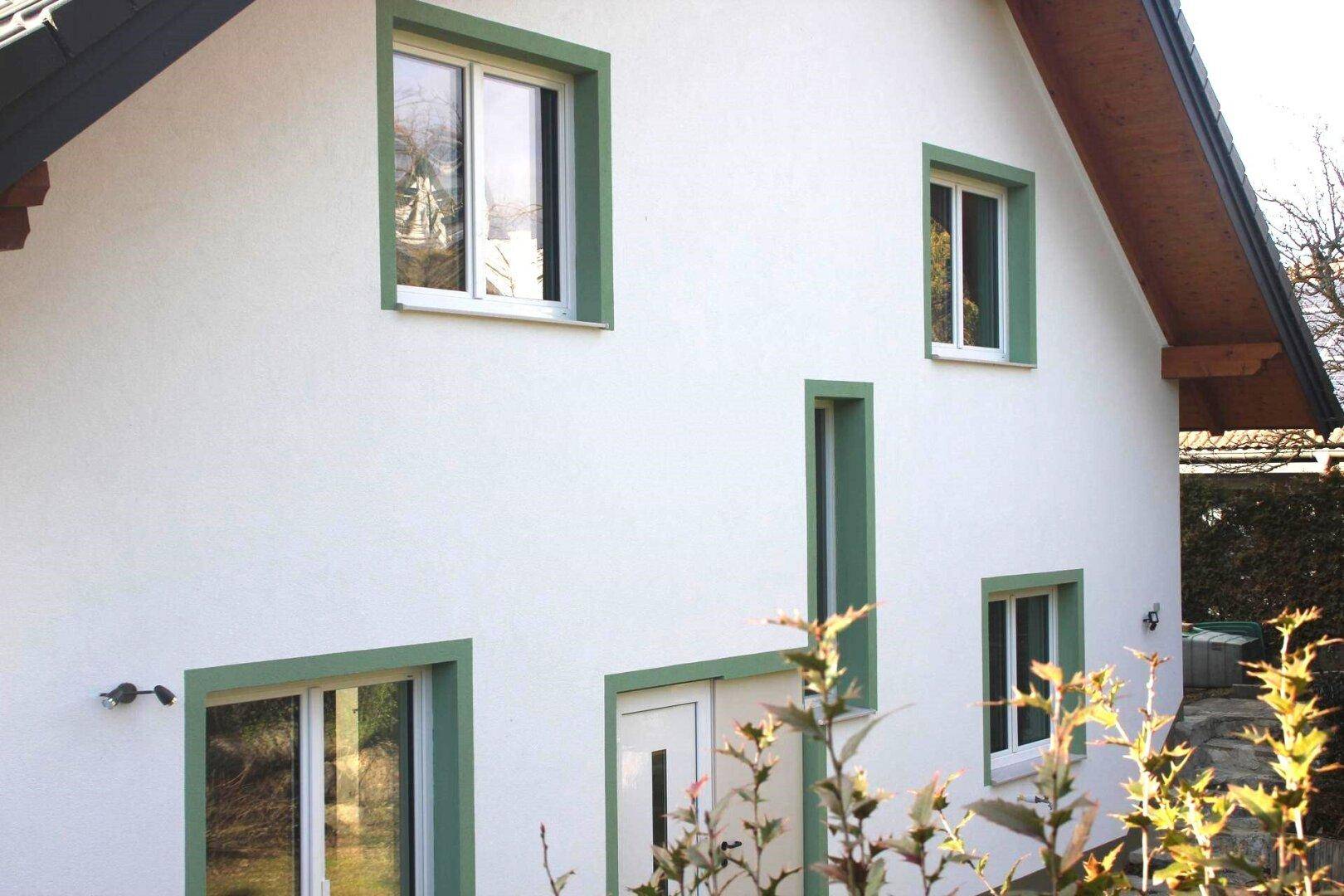 Nahaufnahme der Hausfassade mit weißem Putz, grünen Fensterrahmen und der Eingangstür.