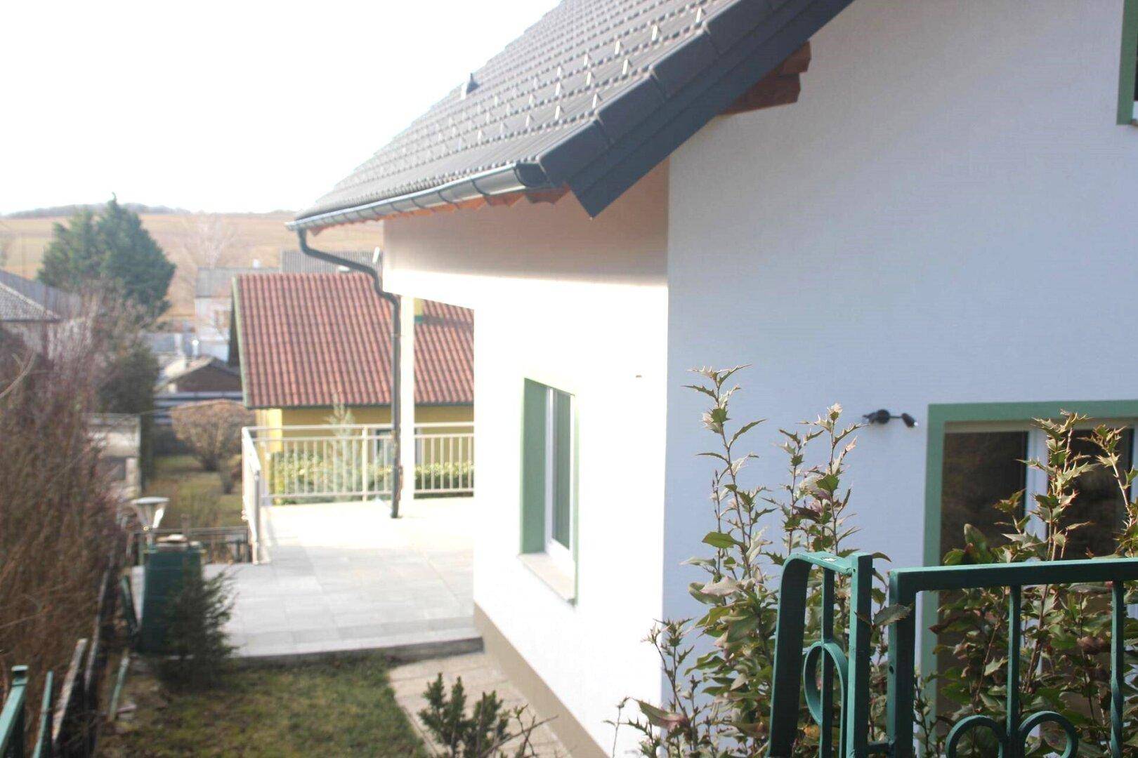 Seitenansicht des Hauses mit gepflastertem Weg und Blick auf die umliegende Landschaft.