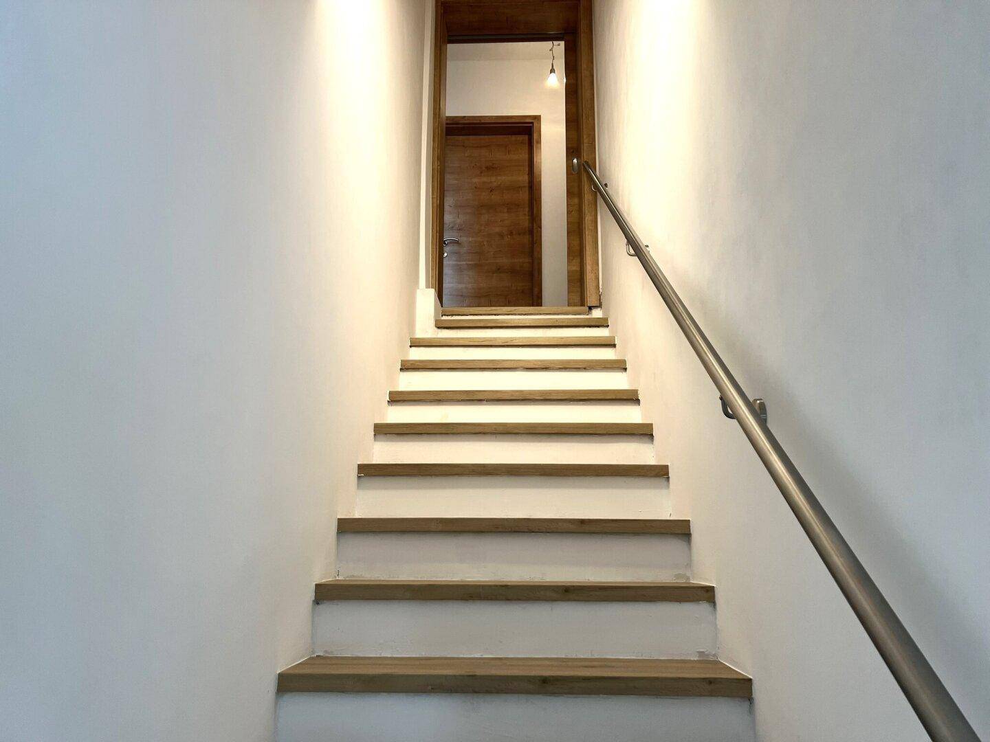 Moderne Treppe mit Holzstufen und weißem Geländer, die zu einer Holztür führt.