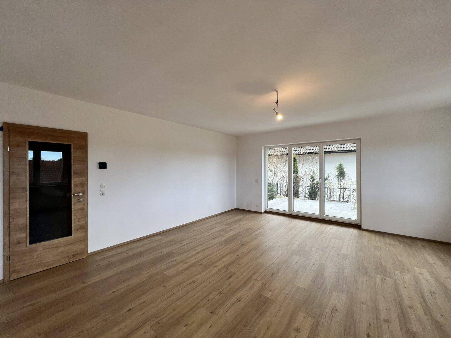 Geräumiges, leeres Zimmer mit Laminatboden und großen Schiebetüren zum Außenbereich.
