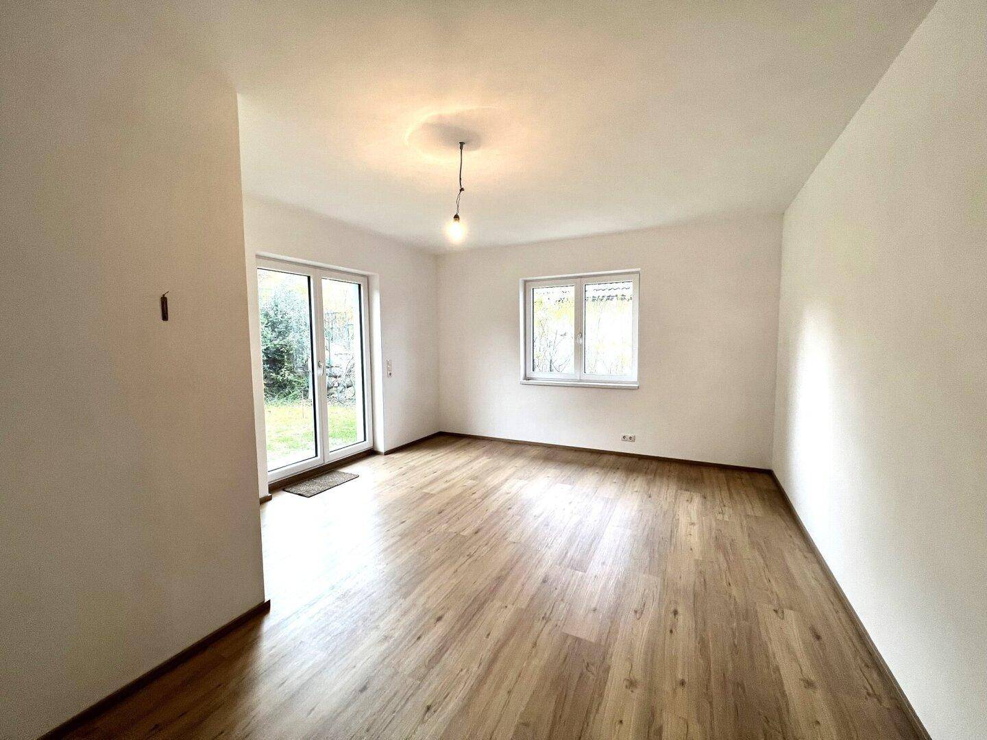 Helles Zimmer mit Laminatboden, weiß gestrichenen Wänden und Zugang zum Garten.