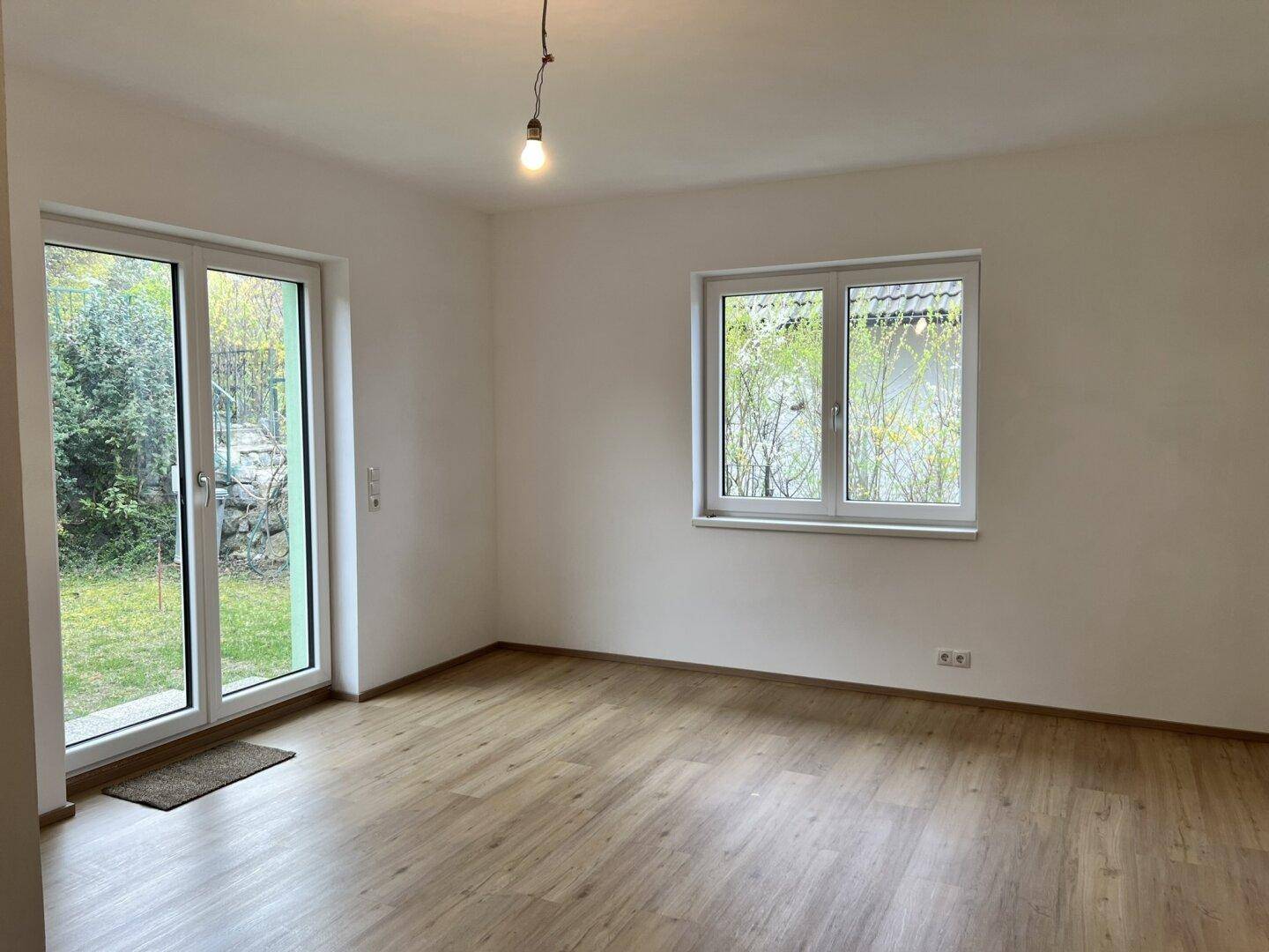 Helles Zimmer mit Laminatboden, weiß gestrichenen Wänden und Zugang zum Garten.