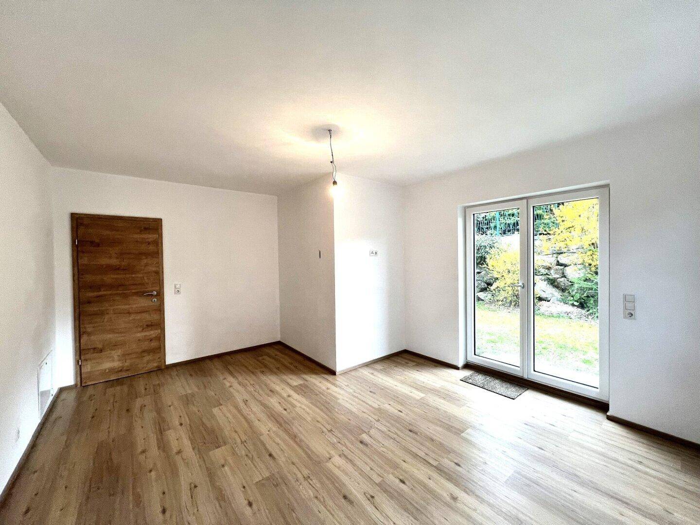Geräumiges Zimmer mit Laminatboden, Holztür und Zugang zu einem sonnigen Außenbereich.