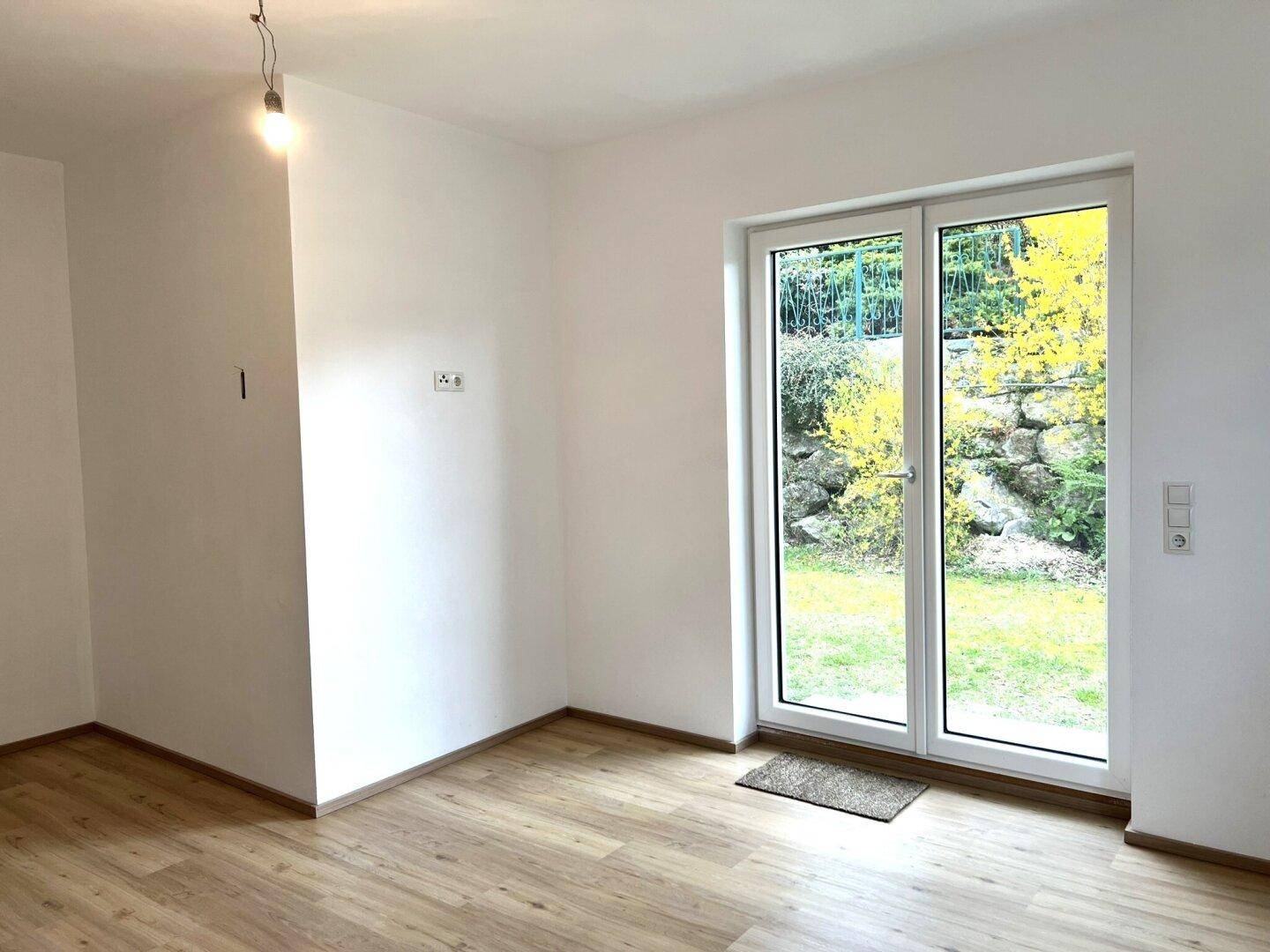 Geräumiges Zimmer mit Laminatboden, weißen Wänden und Zugang zu einem sonnigen Außenbereich.