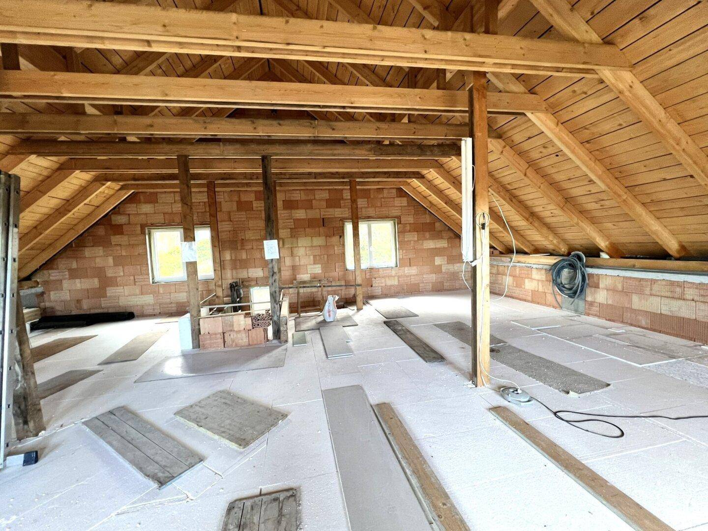 Geräumiger, unausgebauter Dachboden mit Holzdachstuhl und Ziegelwänden, ideal für zukünftige Wohnräume.