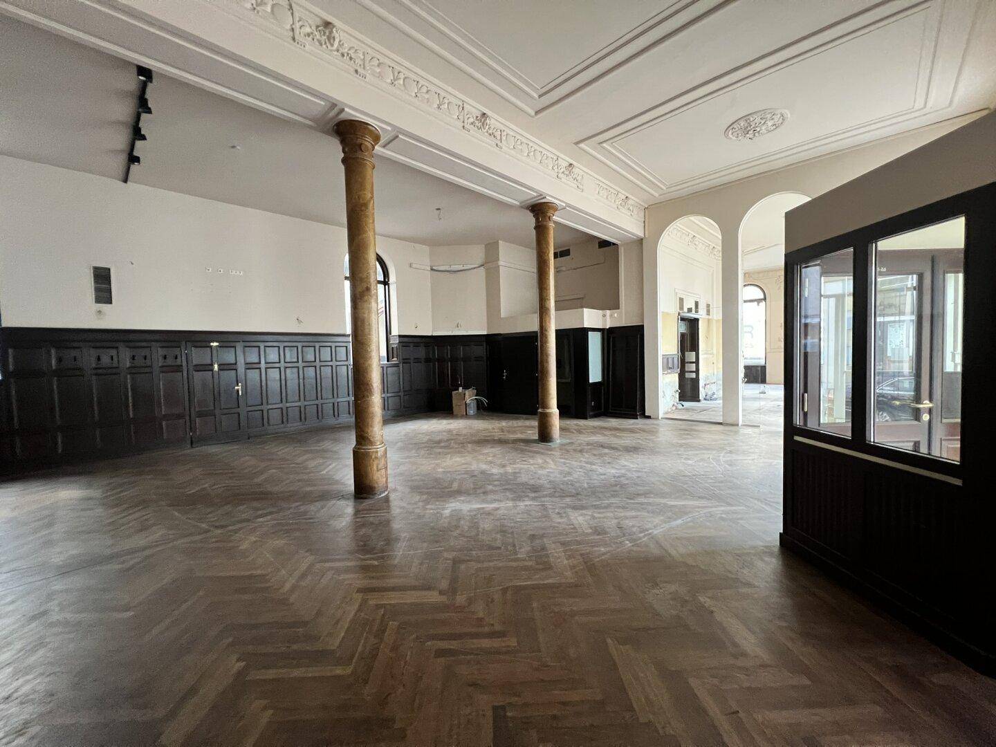 Weitläufiger Innenraum mit hohen Decken, Holztäfelung und zwei markanten Säulen, ideal für gewerbliche Nutzung.