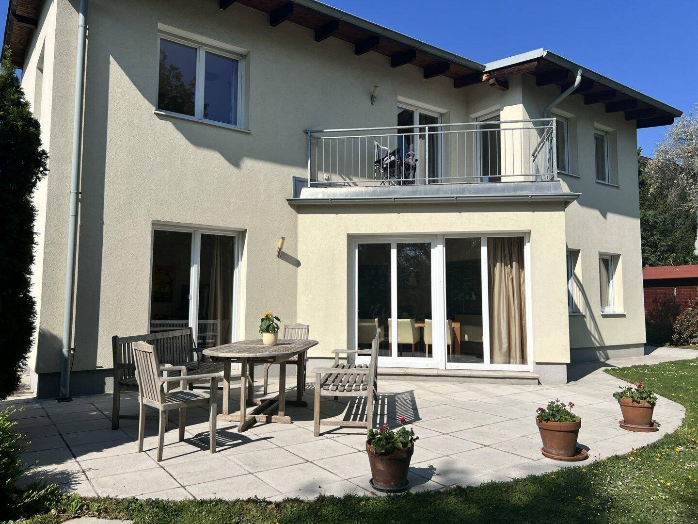 Sonniger Terrassenbereich mit Holztisch und Stühlen, umgeben von Rasen und Blumen.