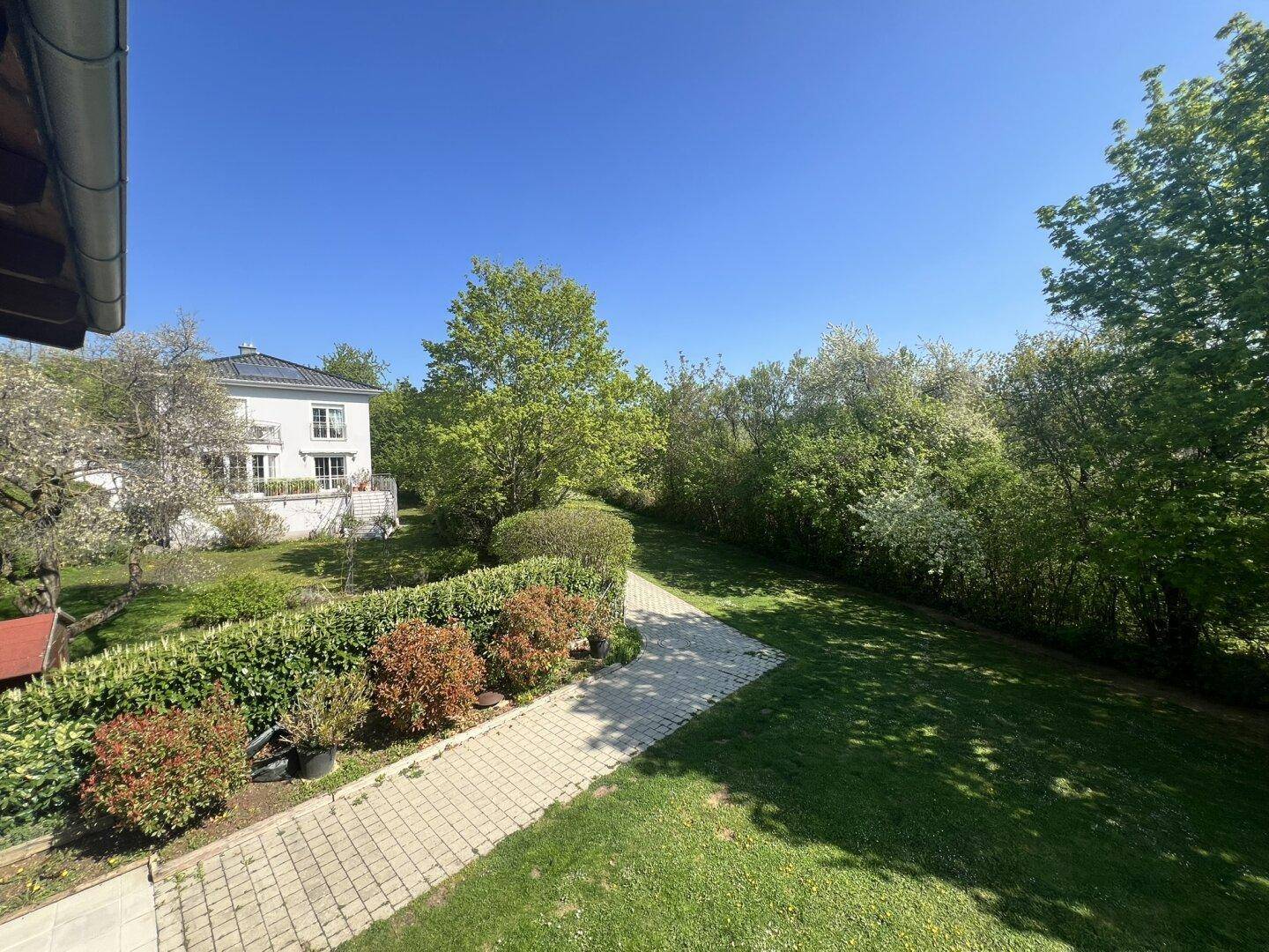 Gepflegter Garten mit Rasenfläche und Hecken, im Hintergrund ein weiteres Wohnhaus.