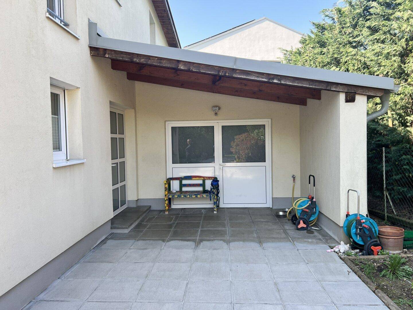 Überdachter Terrassenbereich mit Fliesenboden und Zugang zum Garten, ideal für Entspannung.