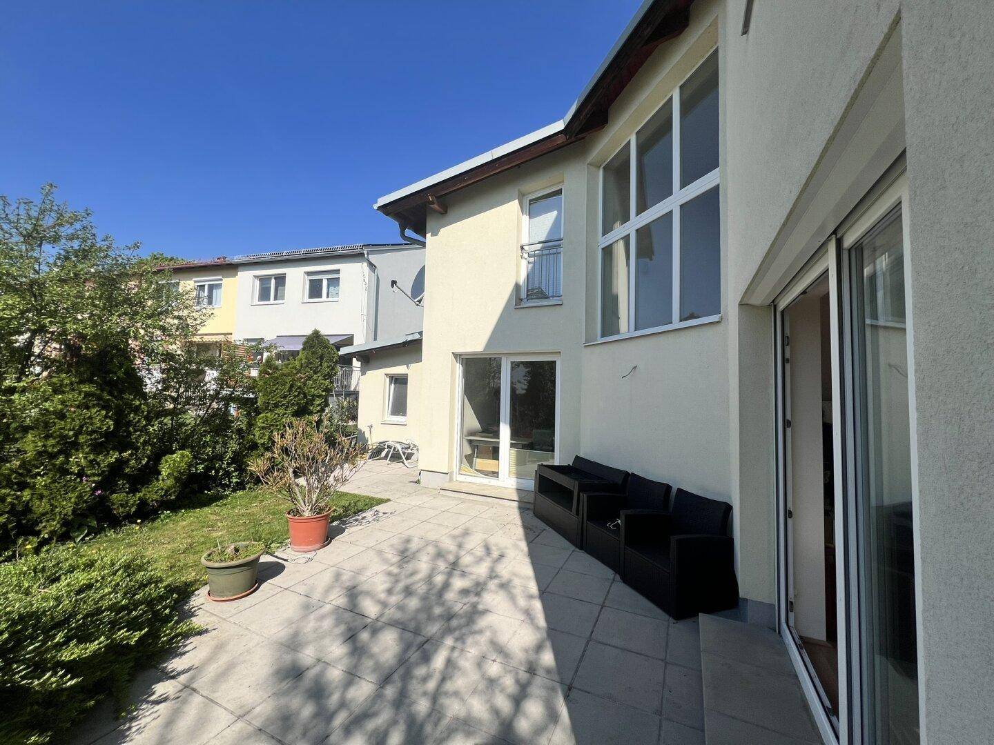 Seitliche Terrasse mit modernen Sitzmöbeln und großen Fenstern zum Garten.