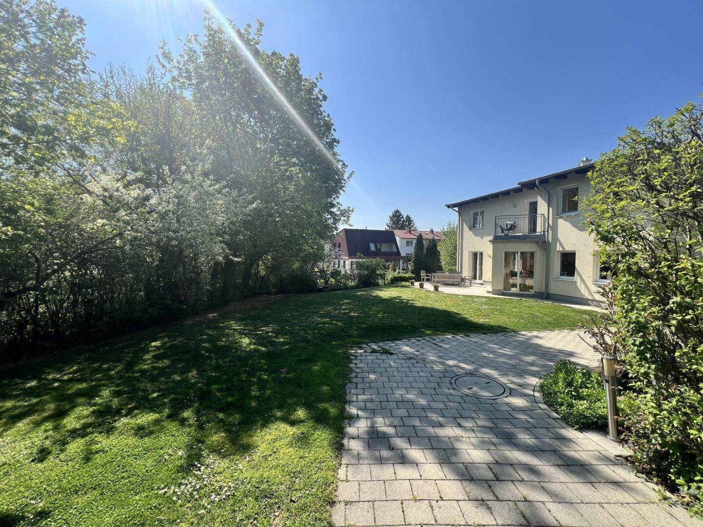 Rückansicht des Hauses mit großer Rasenfläche und gepflastertem Weg an einem sonnigen Tag.