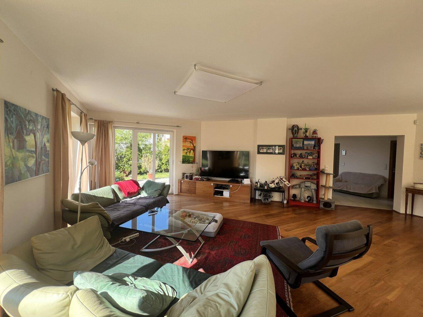 Geräumiges Wohnzimmer mit Holzboden, Fernseher und Zugang zur Terrasse.