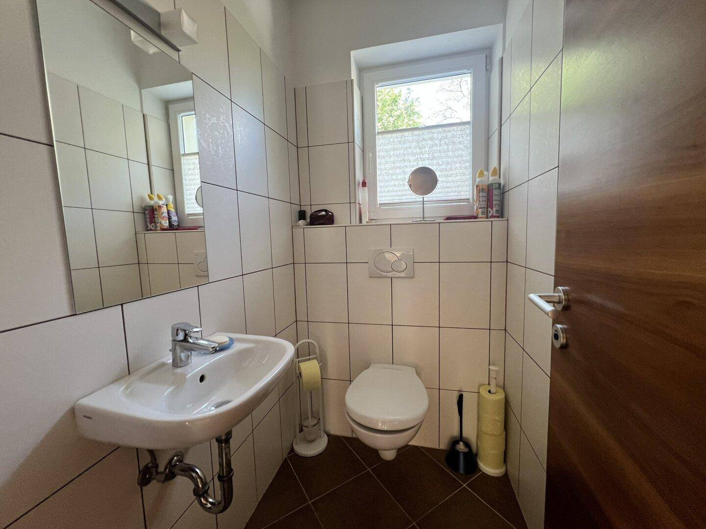 Modern gefliestes Gäste-WC mit Fenster, Waschbecken und Wand-WC.