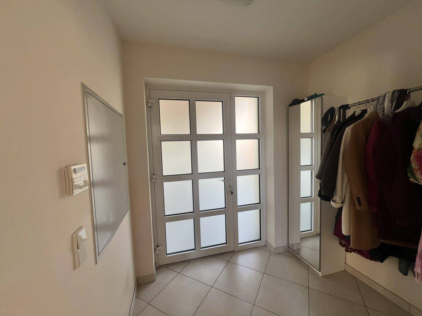 Eingangsbereich mit Fliesenboden, Garderobe und doppelter Glastür.