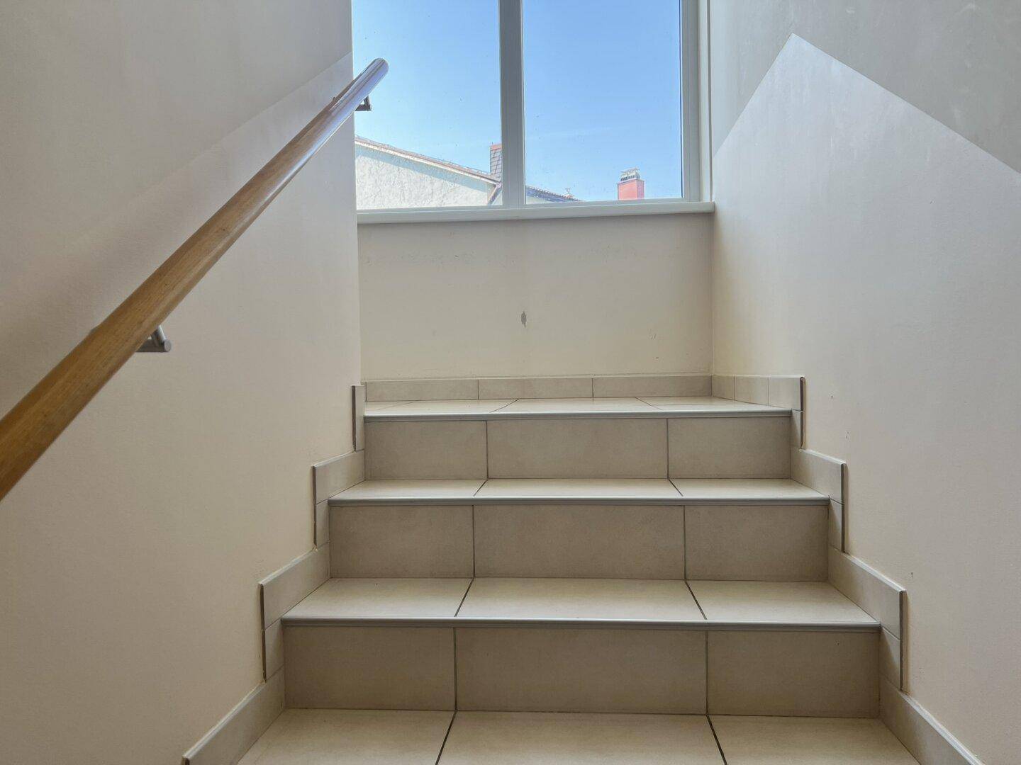 Helle Treppe mit Fliesenstufen und Holzgeländer, führt in das Obergeschoss.