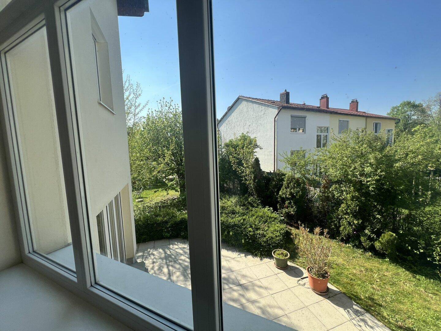 Blick aus dem Fenster auf die Terrasse und den grünen Gartenbereich.