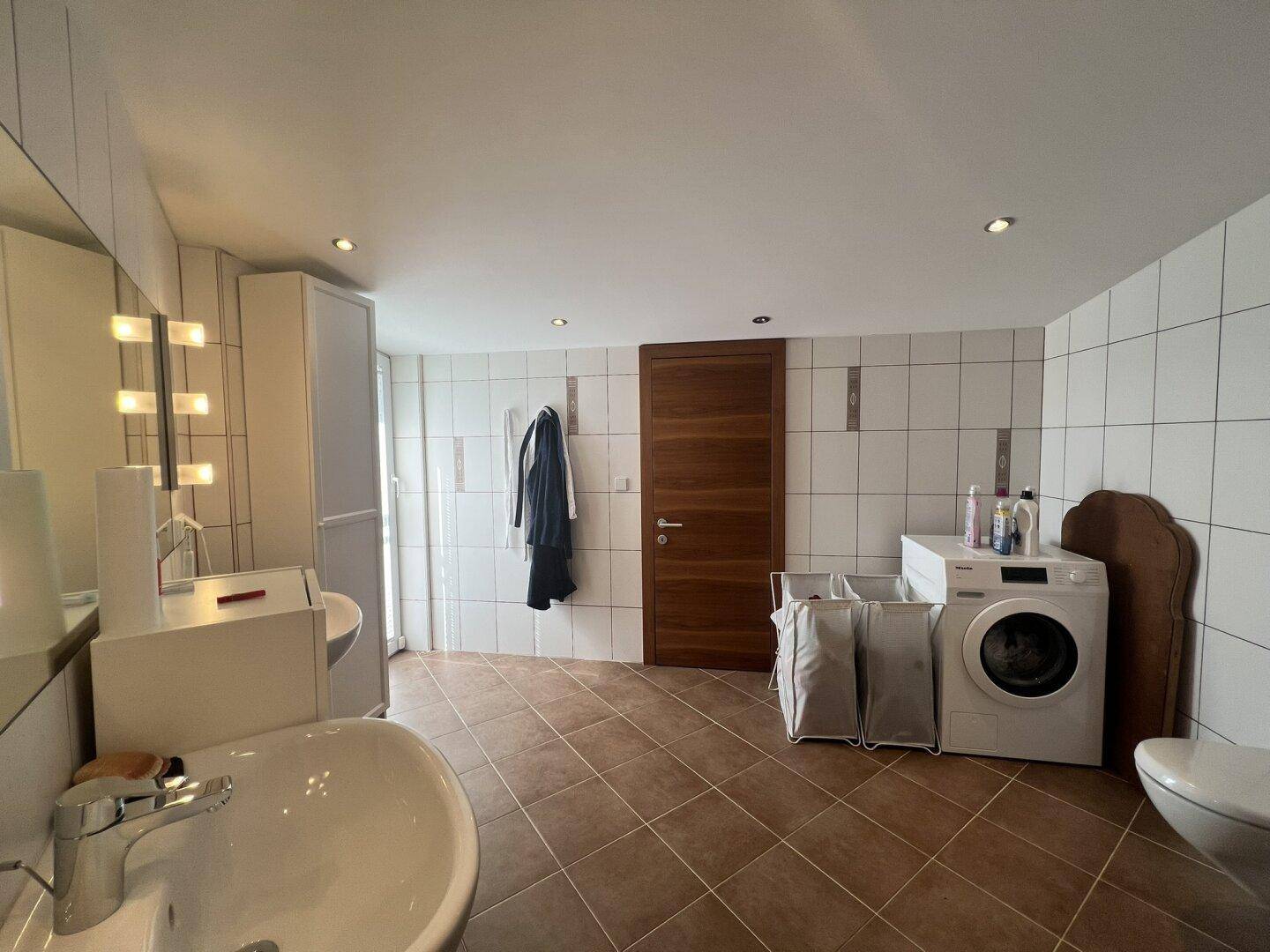 Geräumiges Badezimmer mit Waschmaschine, Doppelwaschbecken und Dusche.