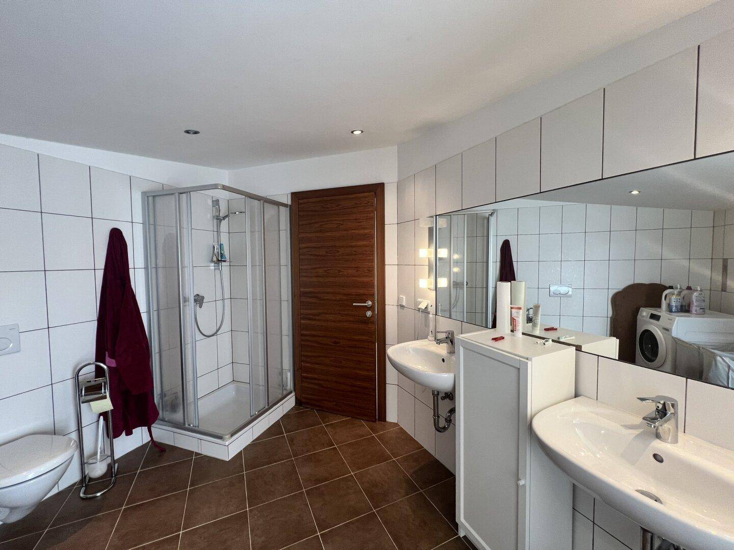 Großes Badezimmer mit Doppelwaschbecken, Dusche und Fliesenboden.