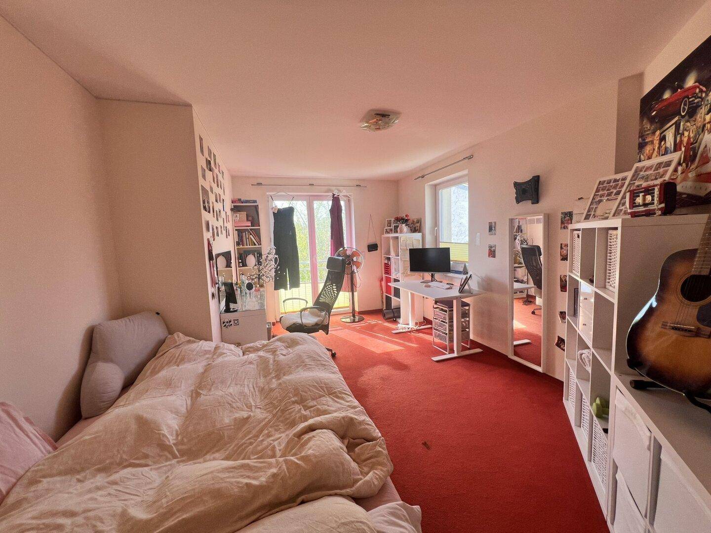 Helles Schlafzimmer mit rotem Teppichboden, Bett und Schreibtisch.