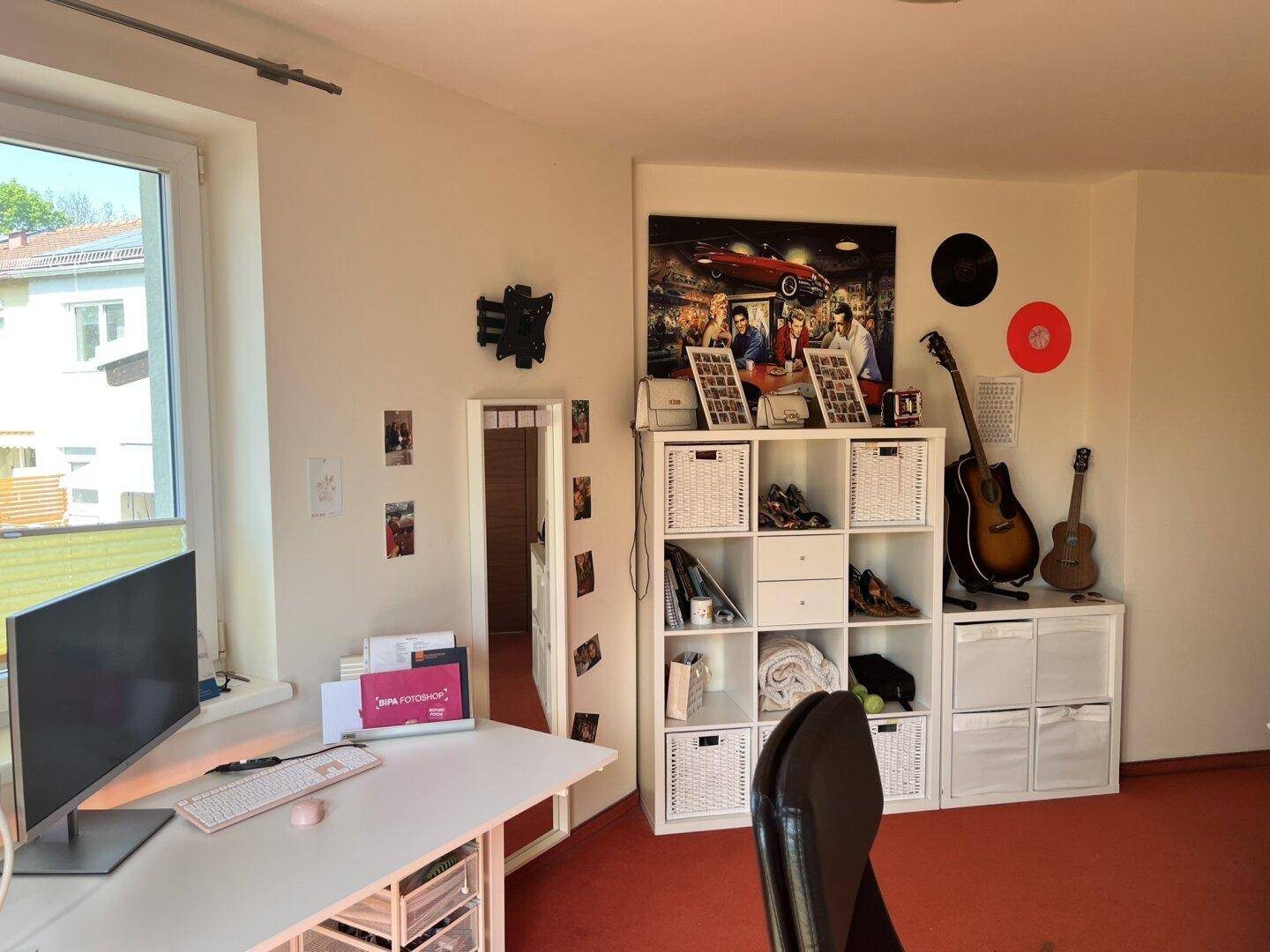Schlafzimmer mit rotem Teppichboden, Schreibtisch und Regalen für Stauraum.