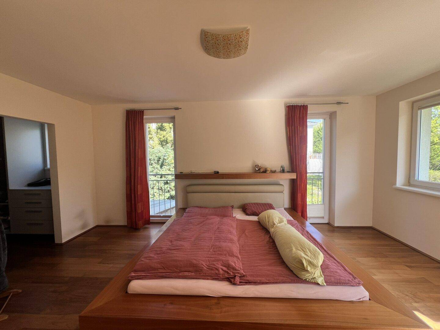 Geräumiges Hauptschlafzimmer mit Holzboden, großem Bett und französischen Balkonen.