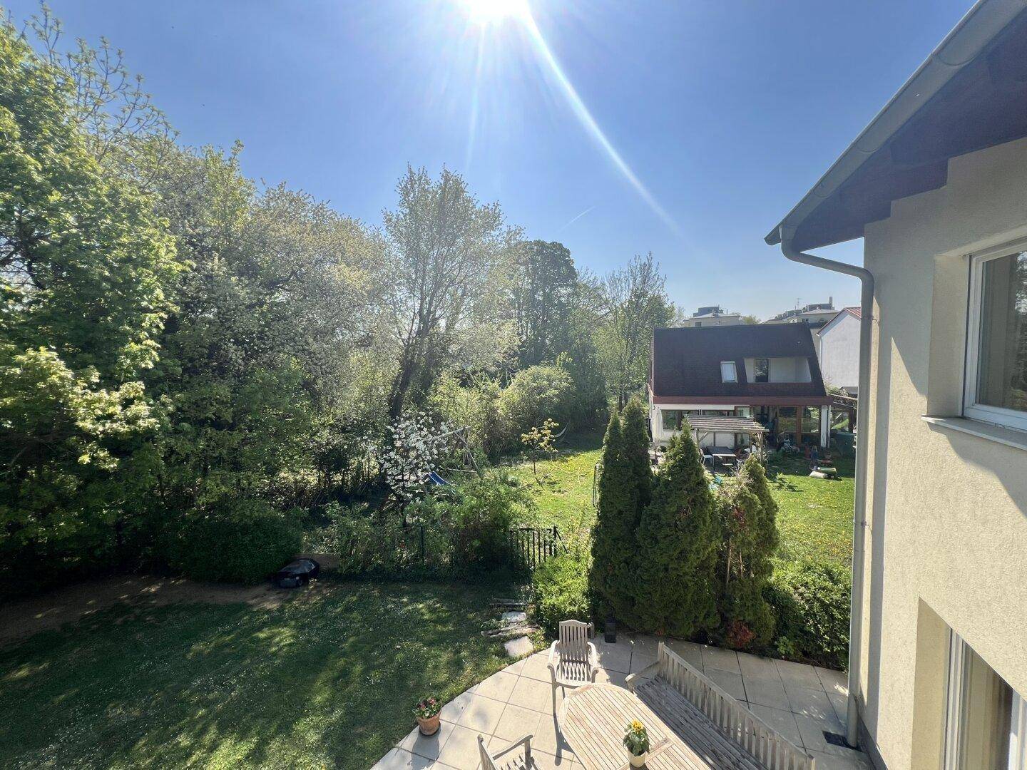 Blick von oben auf den Garten mit Terrasse, Rasen und umliegenden Häusern.
