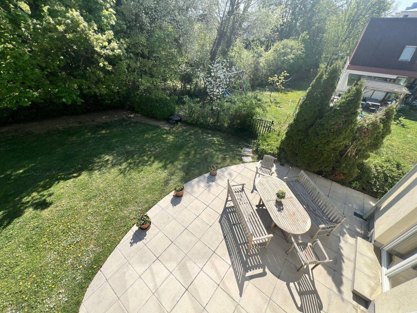 Große gepflasterte Terrasse mit Gartenmöbeln, von oben betrachtet.