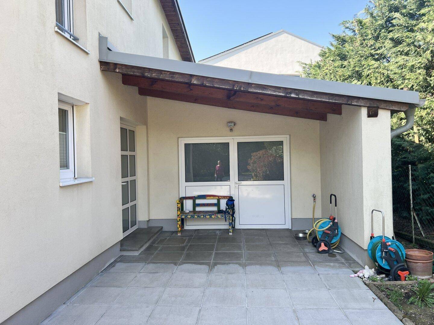 Überdachter Terrassenbereich mit Fliesenboden und Zugang zum Garten, ideal für Entspannung.