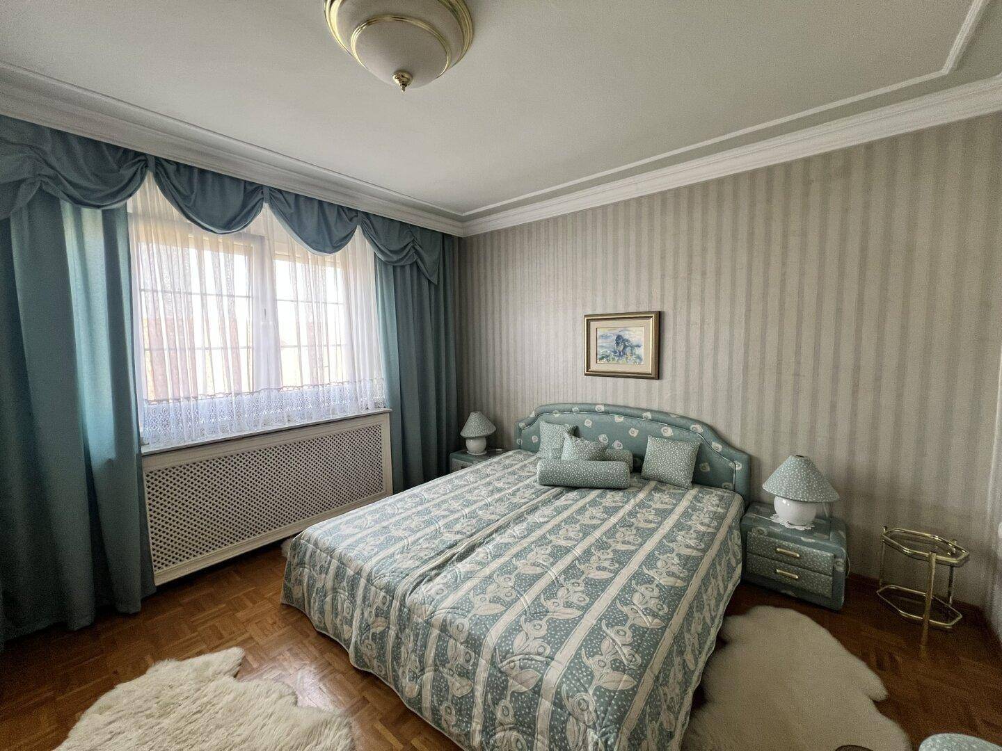 Schlafzimmer mit zwei Einzelbetten, gemusterter Tapete und großen Fenstern mit blauen Vorhängen.