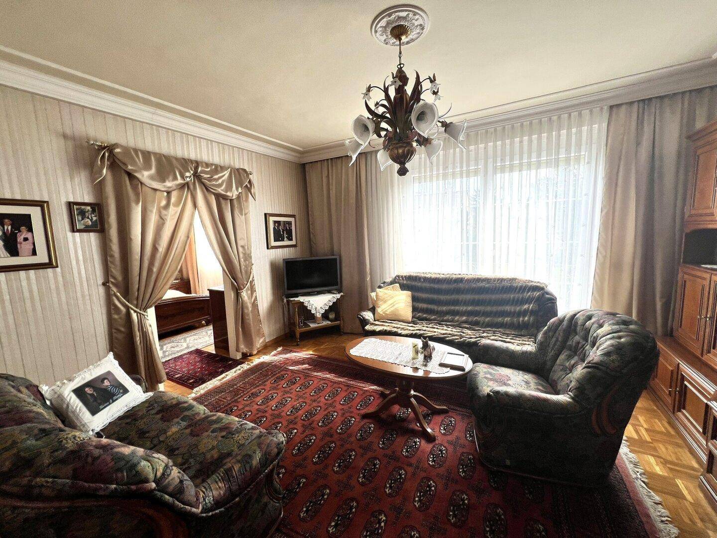 Gemütliches Wohnzimmer mit traditionellen Sofas, Perserteppich und opulenten Vorhängen.