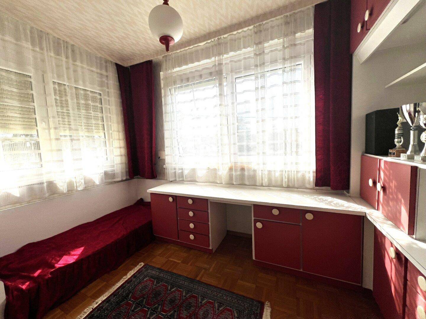Helles Arbeitszimmer mit Schreibtisch, roten Schränken und großen Fenstern.