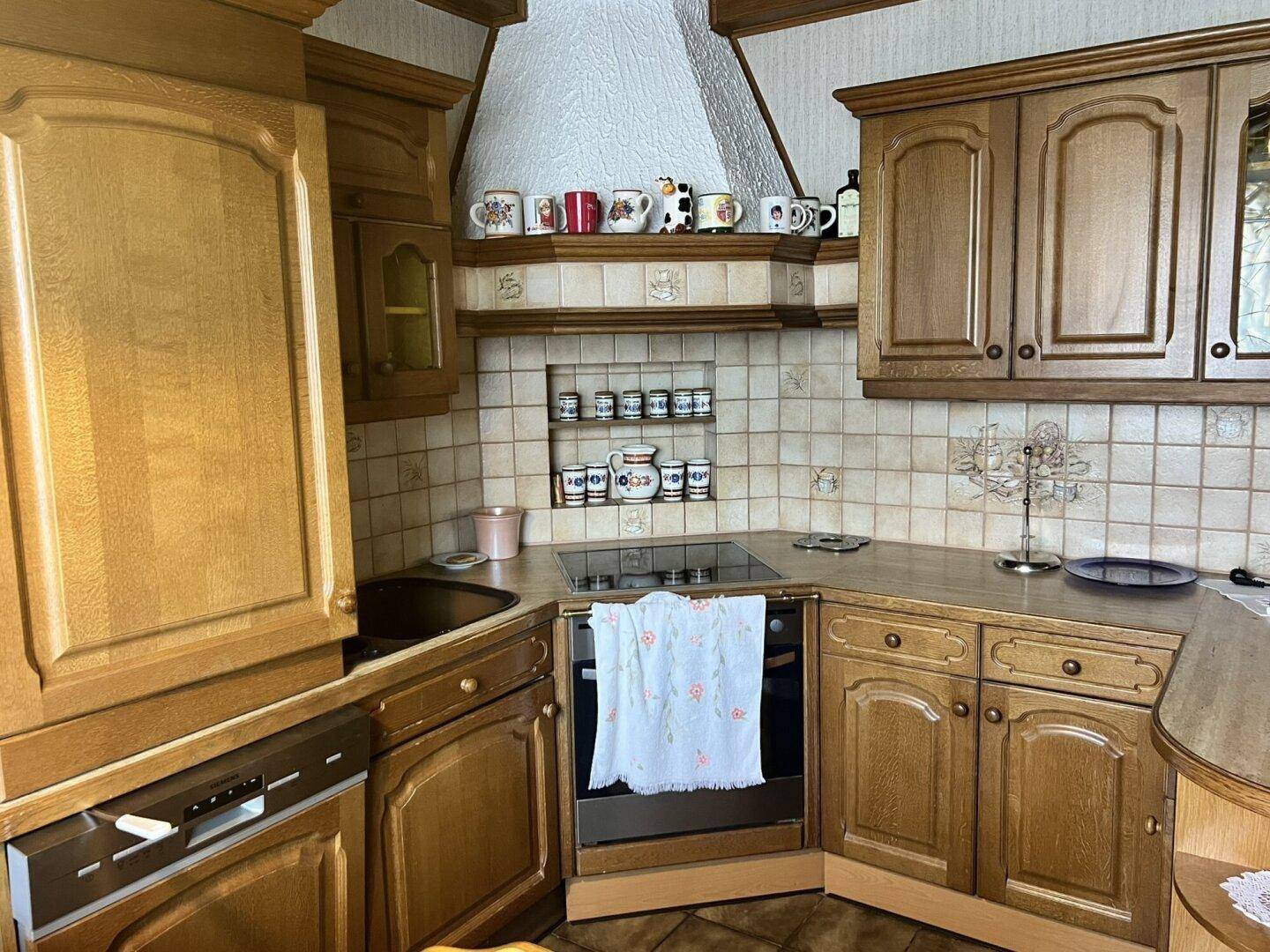 Traditionelle Küche mit Holzschränken, gefliestem Spritzschutz und integrierten Elektrogeräten.