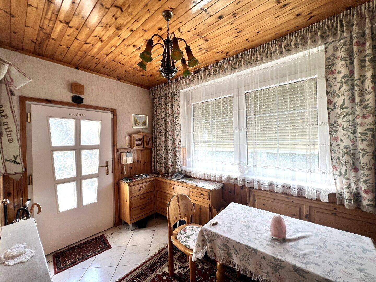 Kleiner Essbereich mit Holztäfelung an der Decke, Fliesenboden und einem Fenster mit Jalousien.