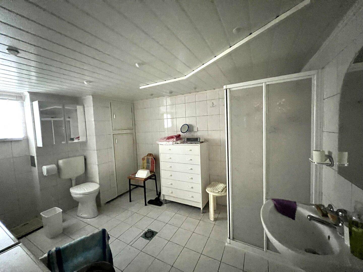 Badezimmer im Untergeschoss mit weißen Fliesen, Duschkabine, Toilette und Waschbecken.