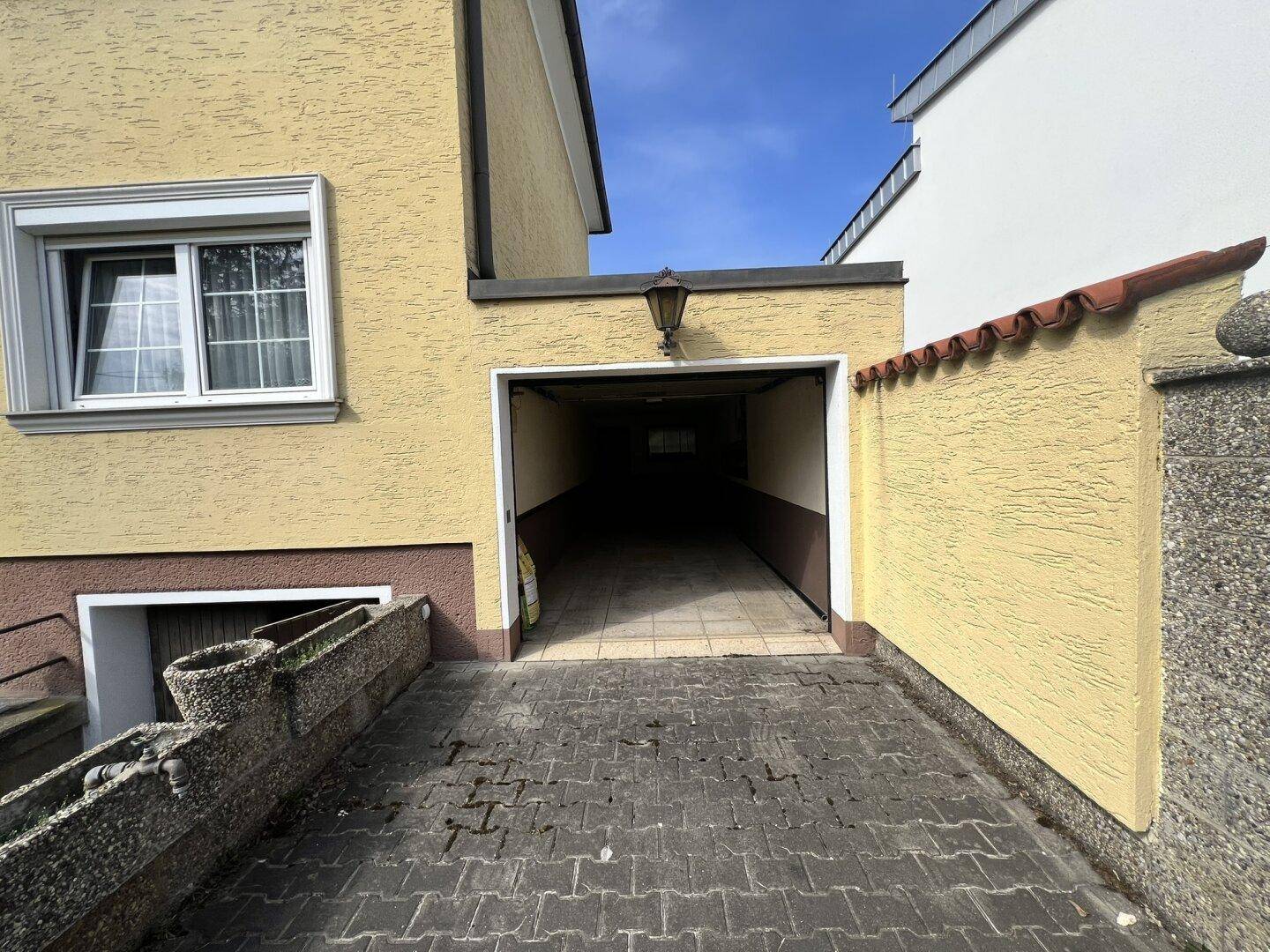 Einfahrt zu einer dunklen Garage am gelben Haus mit Ziegeldach.
