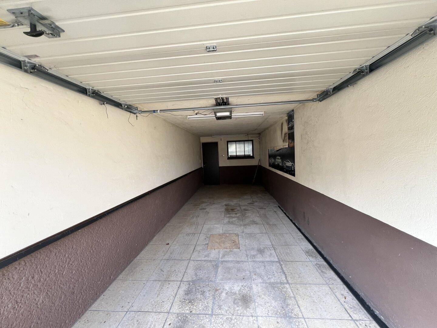 Lange, leere Garage mit gefliestem Boden und einem kleinen Fenster im hinteren Bereich.