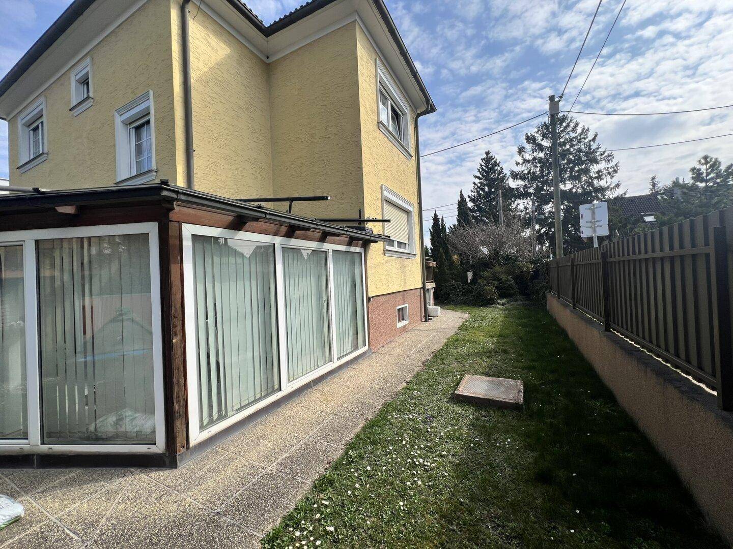 Seitenansicht des gelben Hauses mit Wintergarten und einem Rasenweg daneben.