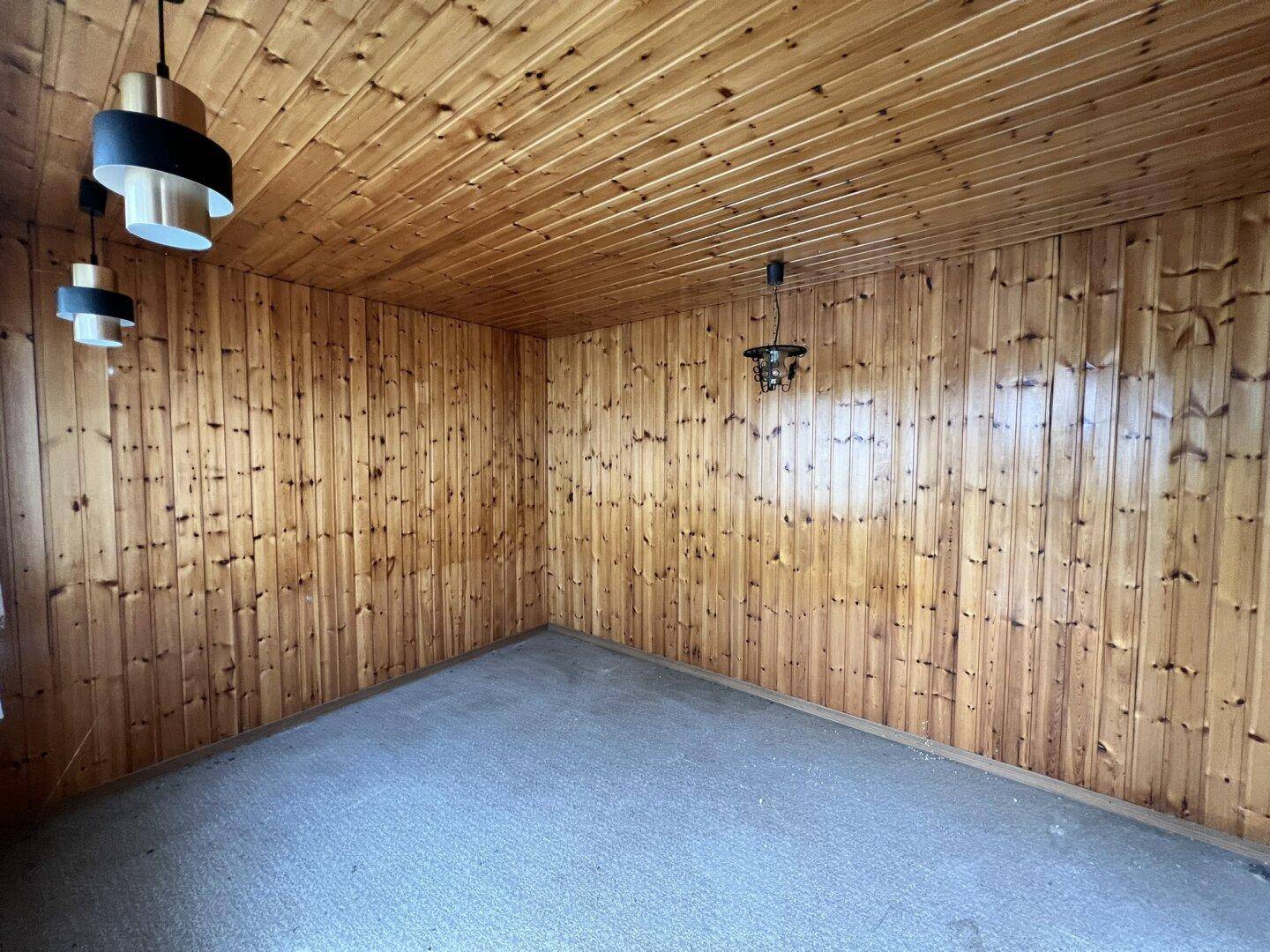 Raum mit holzvertäfelten Wänden und Decke sowie Teppichboden und modernen Lampen.