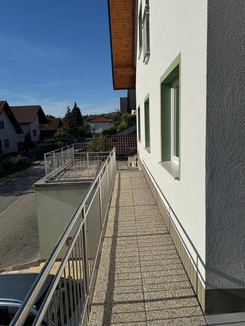 Langer, schmaler Balkon mit modernen Metallgeländern entlang der Hausfassade unter blauem Himmel.